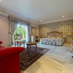 Dormitorio principal con cama de matrimonio, mobiliario clásico y salida al jardín en vivienda de La Costa del Sol