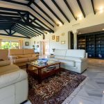 Amplio salón con techos altos, vigas de madera, sofás de piel y luz natural en vivienda de lujo en La Costa del Sol